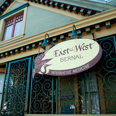 Outside the Victorian style building of East West SF in the Bernal neigborhood of San Francisco. Logo out front says East West Bernal Integrative Medicine